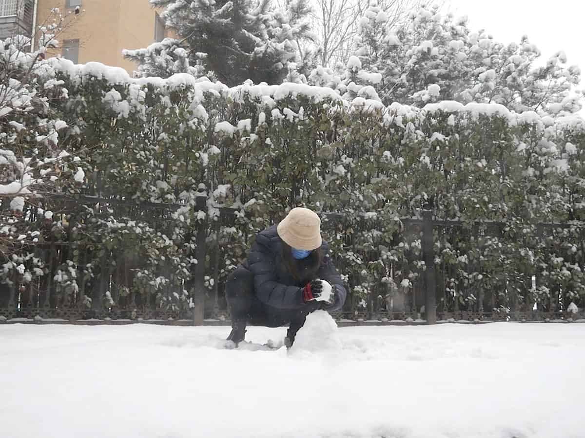 still from video of woman wearing a face mask in the snow making a small snowman.