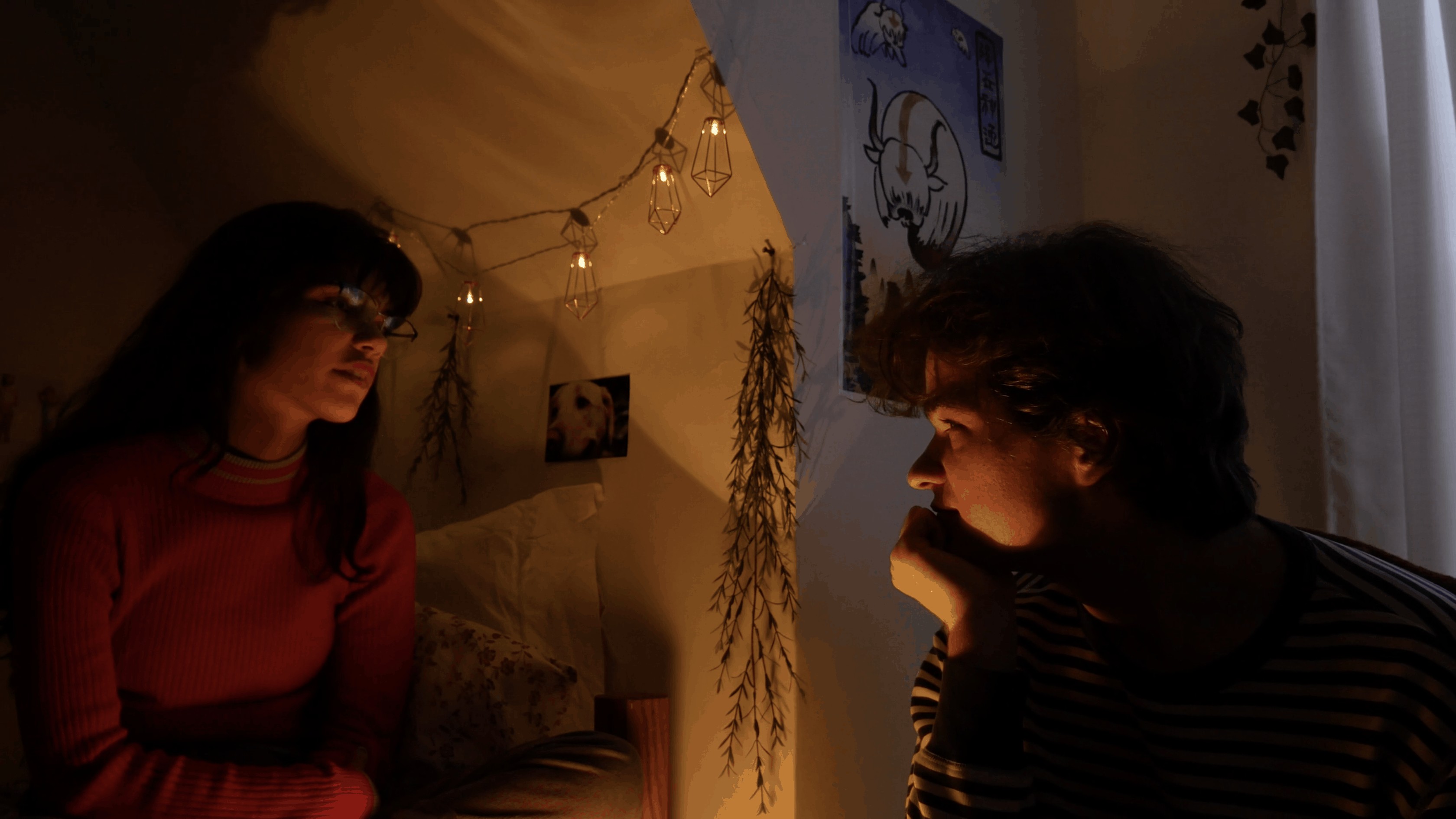 still image from video of two people facing each other in a white room lit with string lights