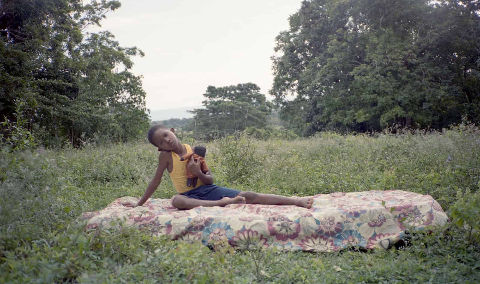 film still of a field of wildflowers, a child holding a doll.